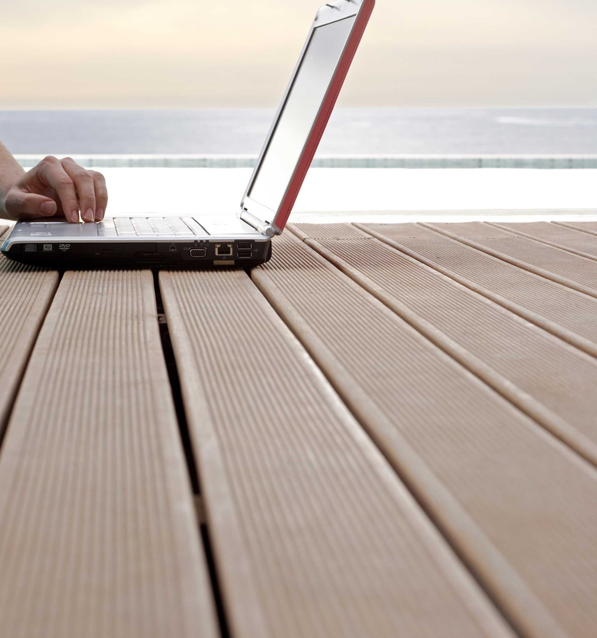 Hand bedient Laptop der auf Terrassendielen steht